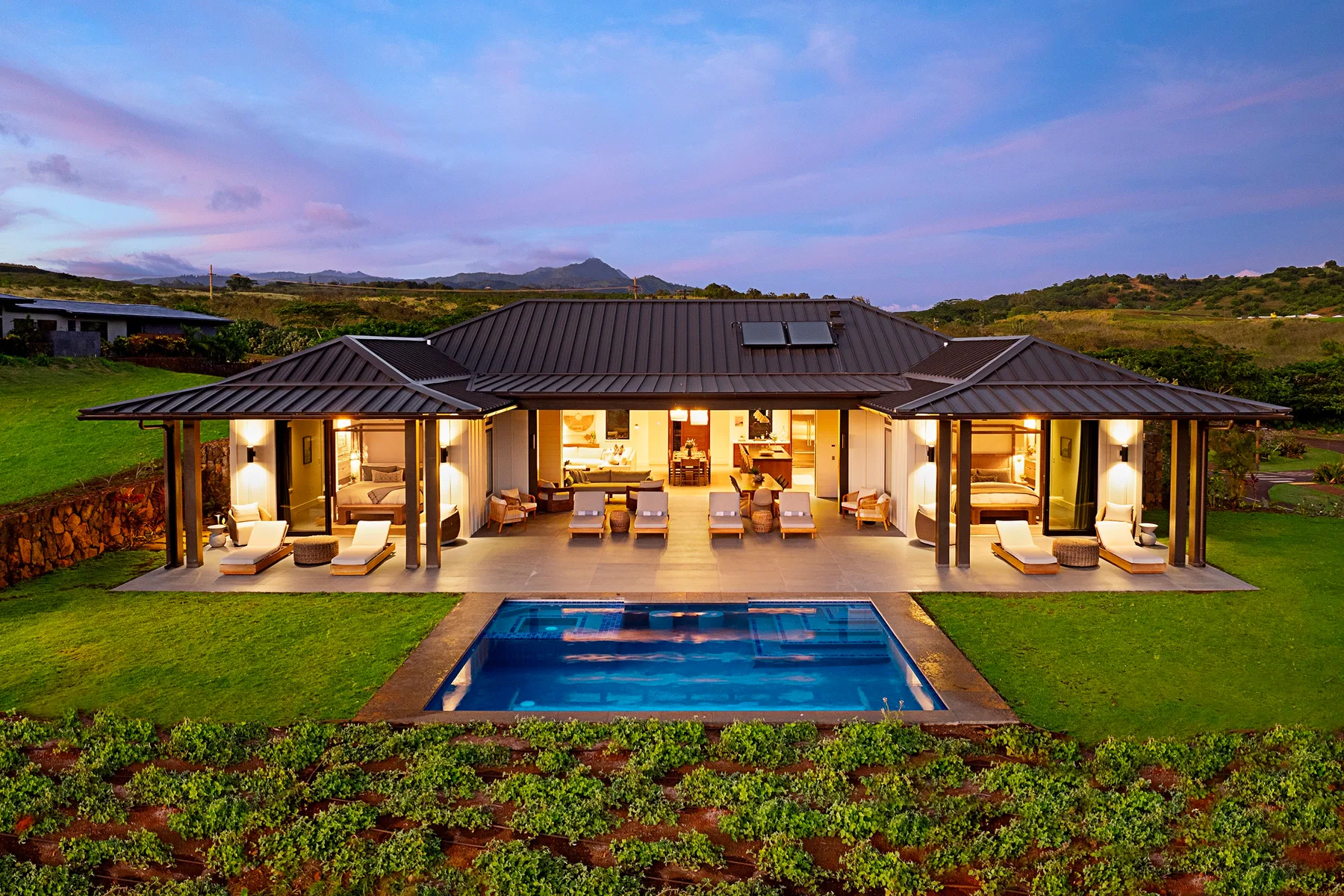 A modern house opens onto a lawn and swimming pool beneath a colorful evening sky.