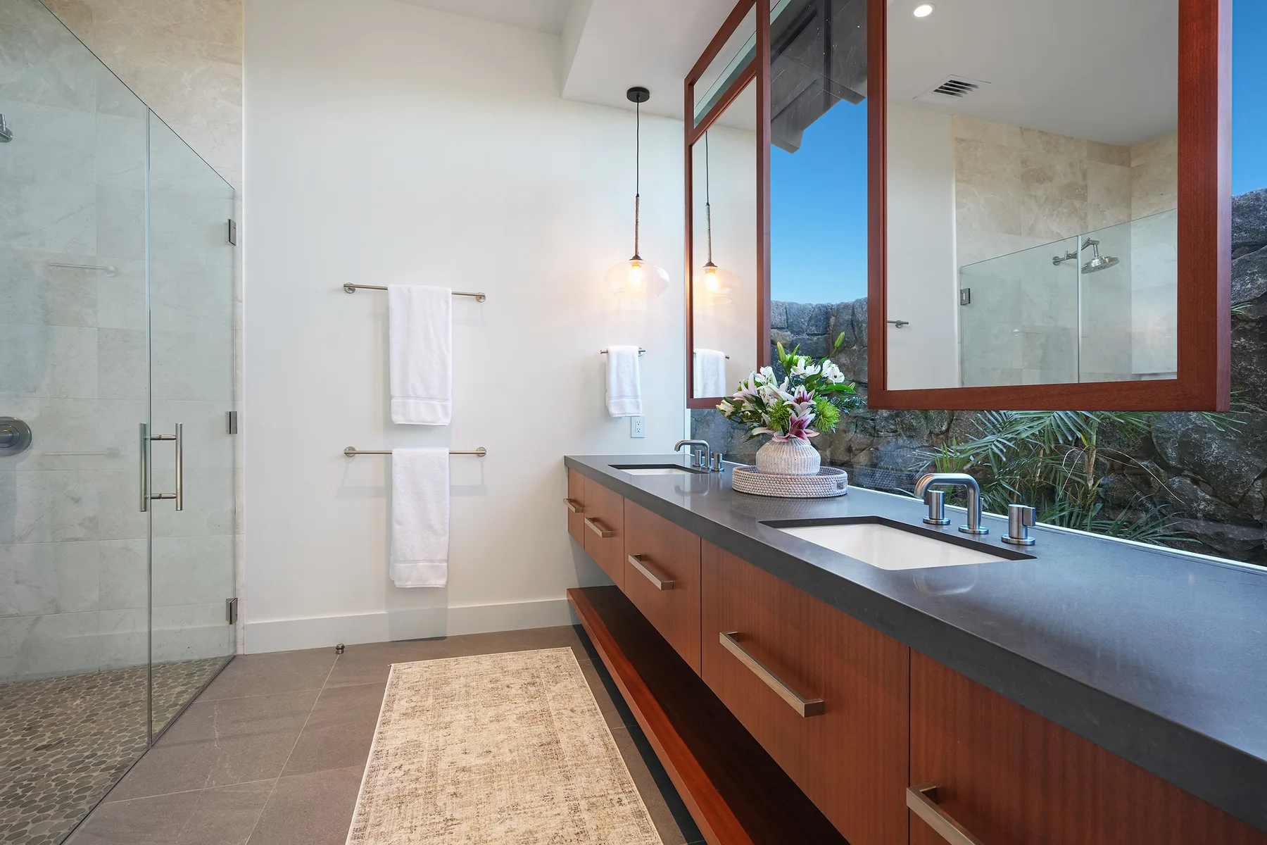 A bathroom with a glass shower, double sinks, and a long vanity.