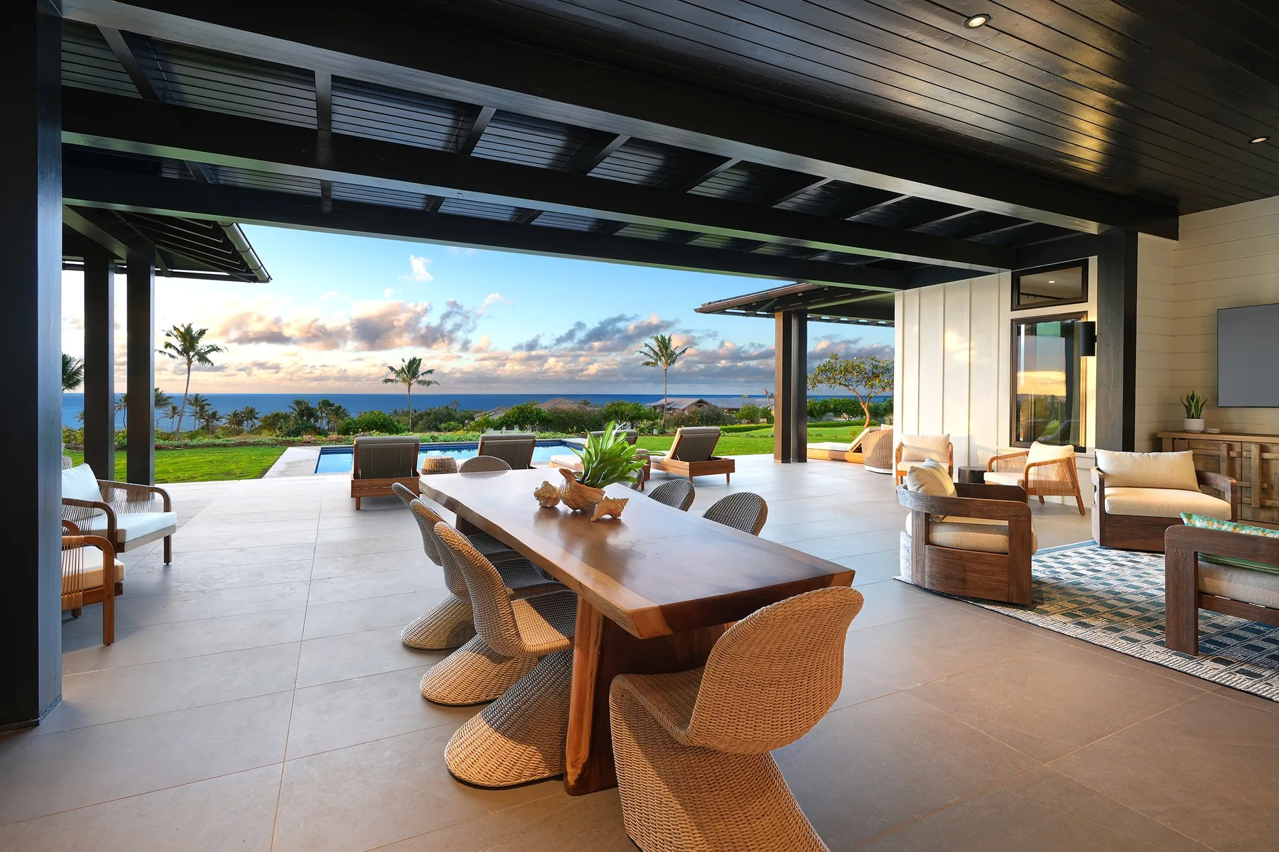 An open-air dining area overlooks a pool, landscaped grounds, and the ocean.