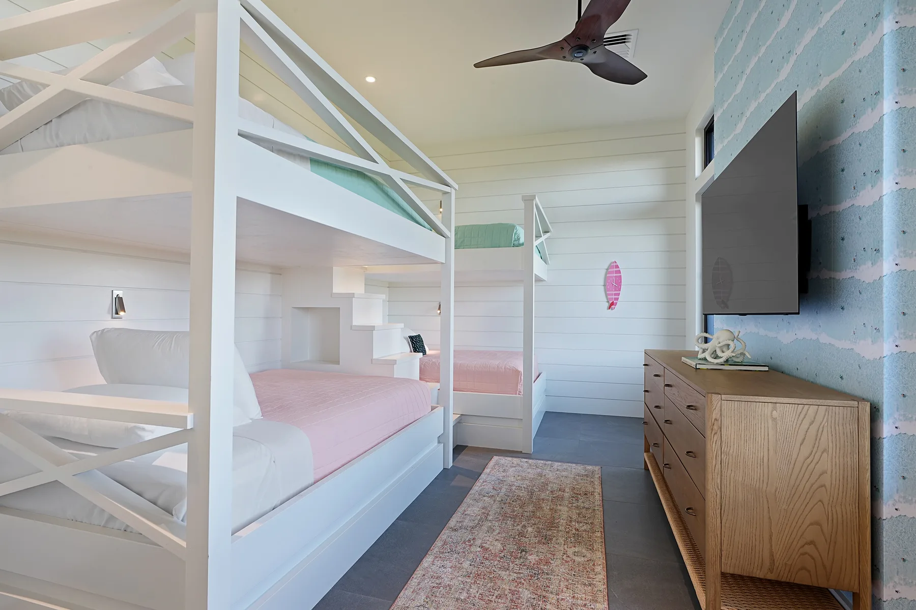 A bunk bedroom with white bunk beds, pink bedding, and a dresser.