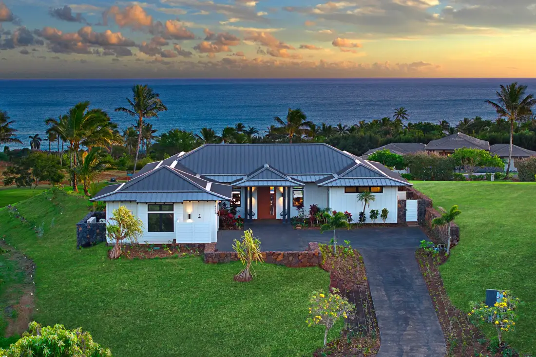 A single-story house stands on a green lawn beside the ocean.