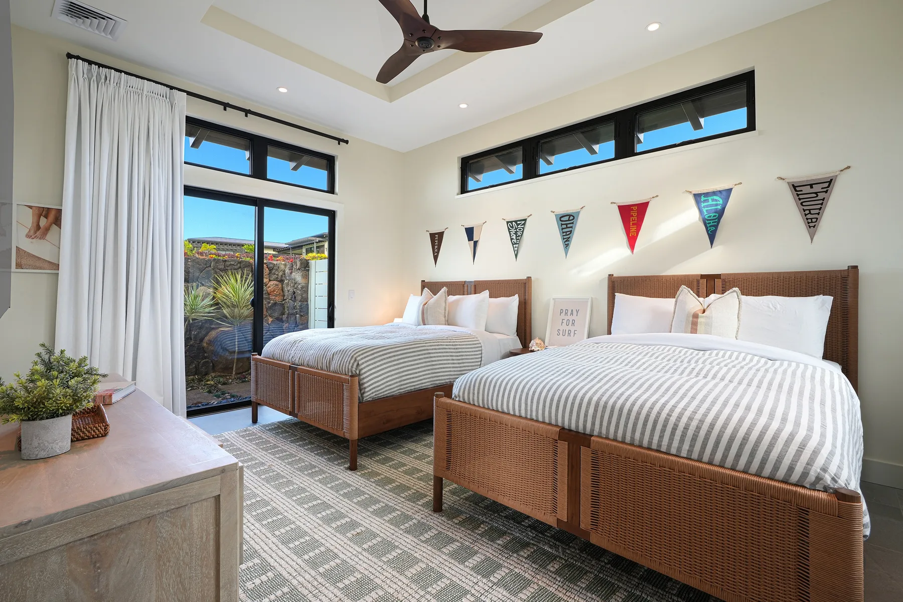 A bright bedroom with two beds, striped bedding, and a ceiling fan.