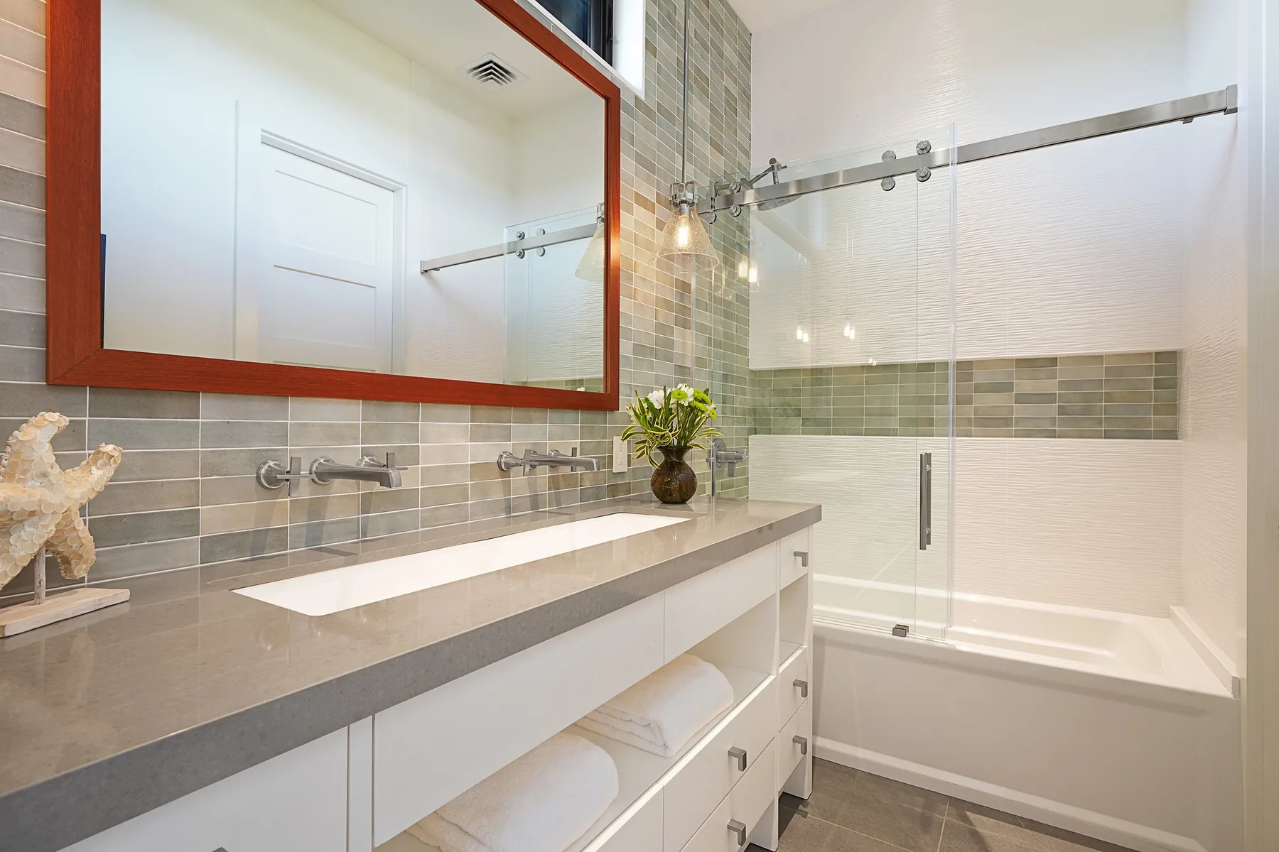A bright bathroom with a long vanity, mirror, and glass shower.
