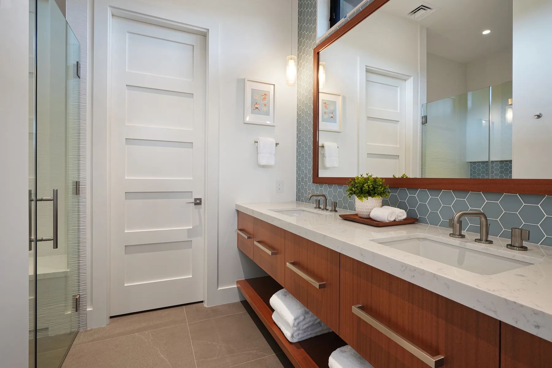 A bright bathroom with a long vanity, large mirror, and glass shower.