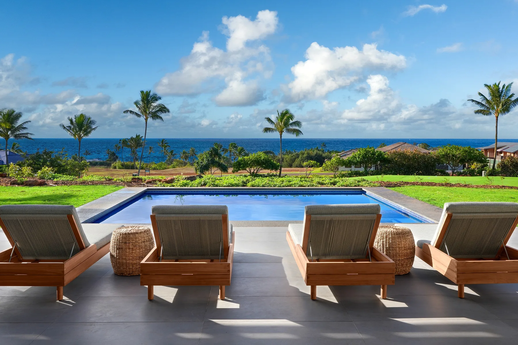 Poolside seating overlooks the ocean, with palm trees along the shore.