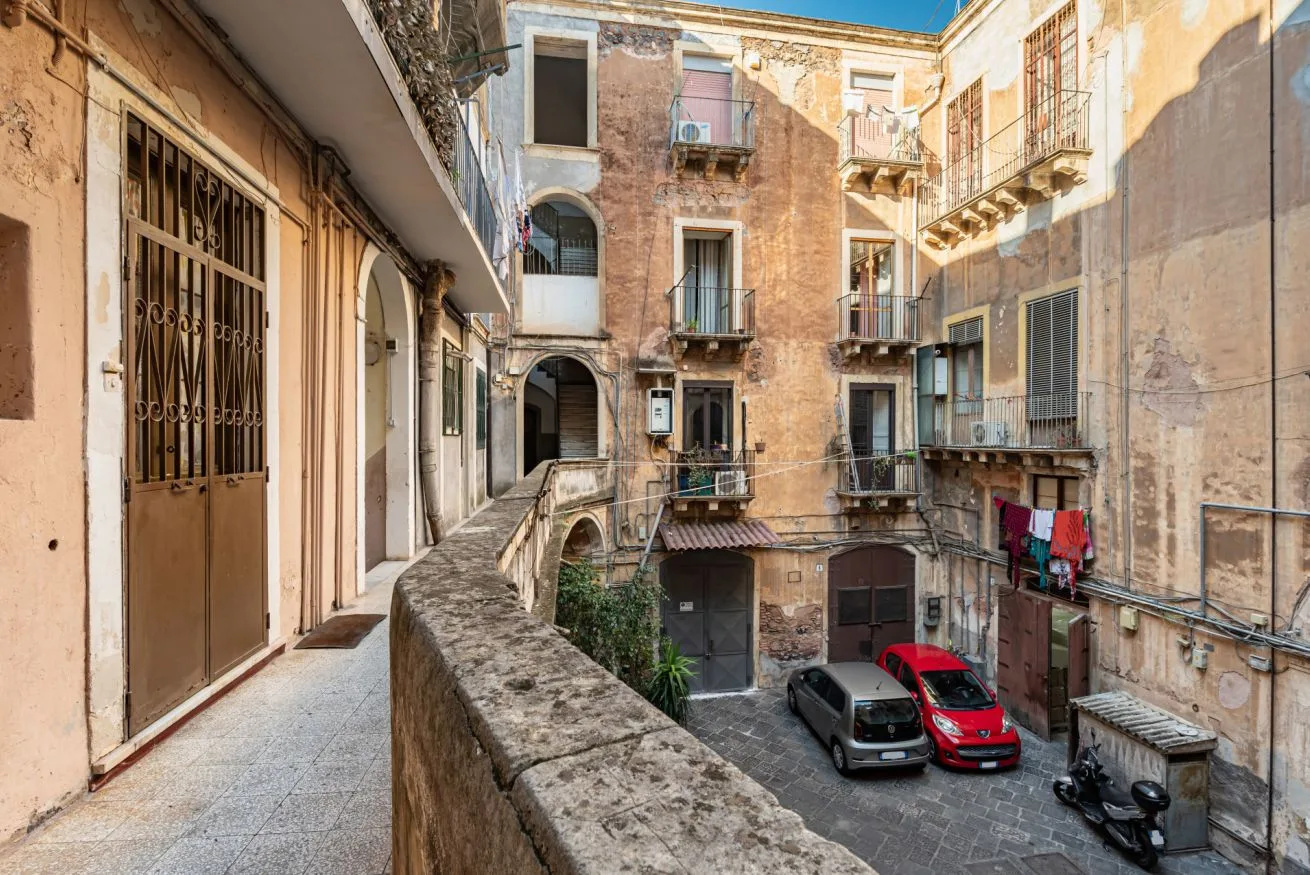 An enclosed courtyard surrounded by weathered apartment buildings, with parked cars below.