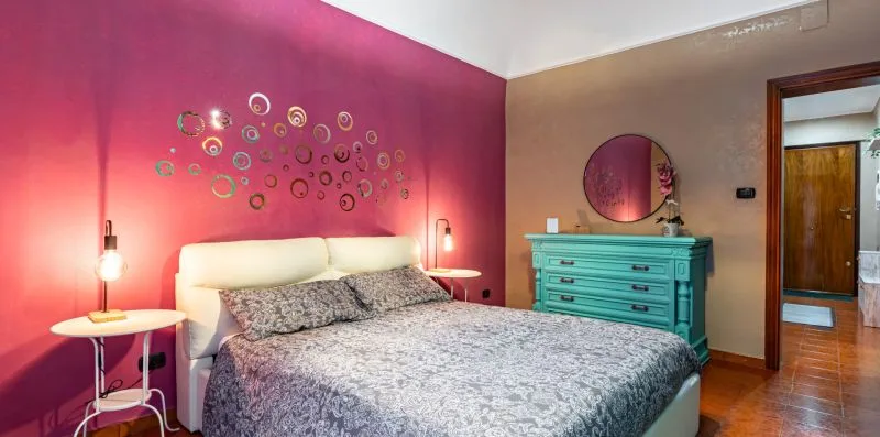 A bedroom with a bed, turquoise dresser, and colorful circular wall decor.