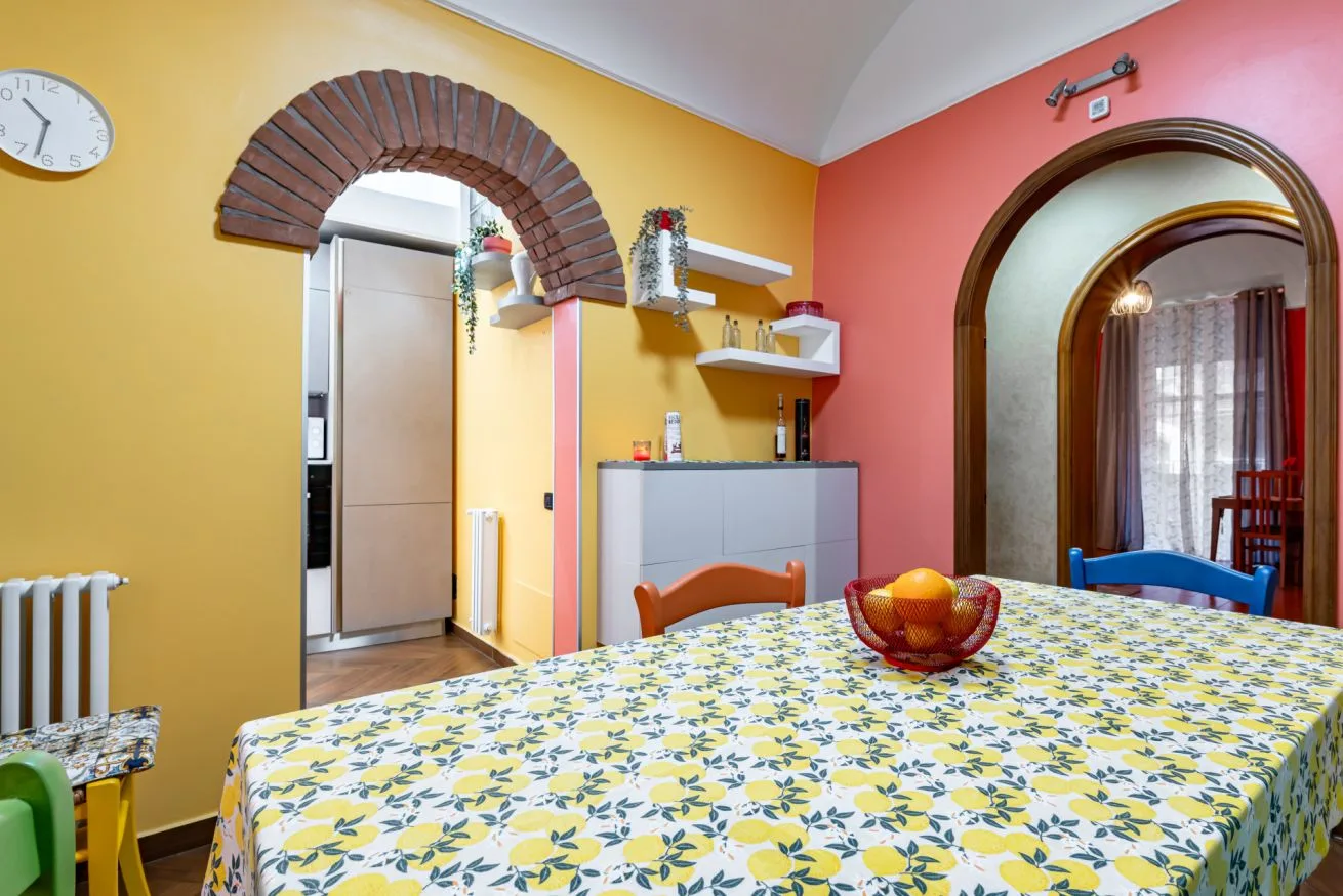 A dining area with a patterned tablecloth and a bowl of fruit on the table.