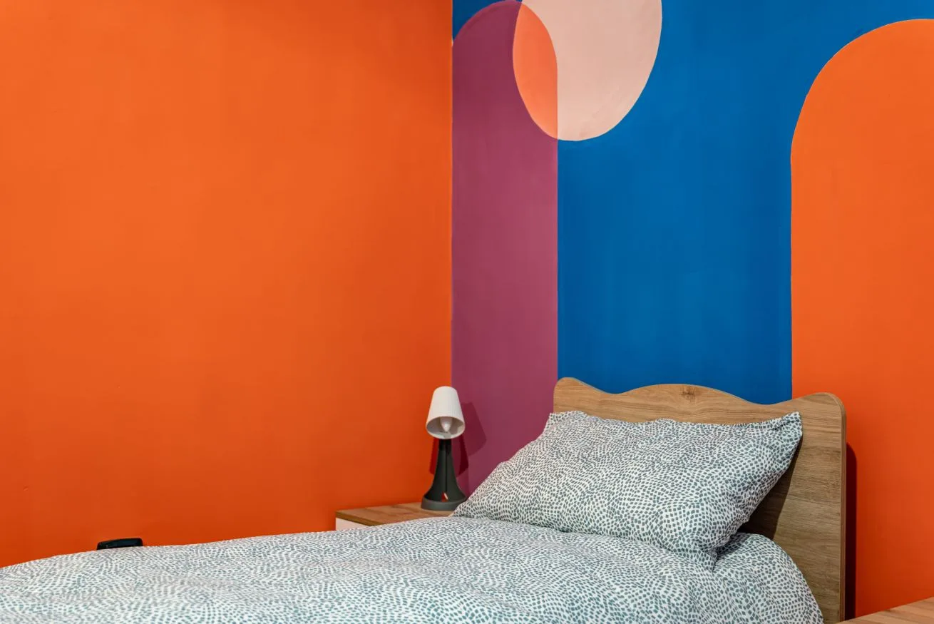 A bedroom with a bed against a colorful wall.