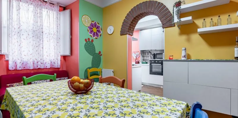 A colorful dining area opens into a kitchen, with a patterned tablecloth.