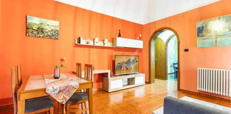 A bright living room with orange walls, wooden dining furniture, and a television.