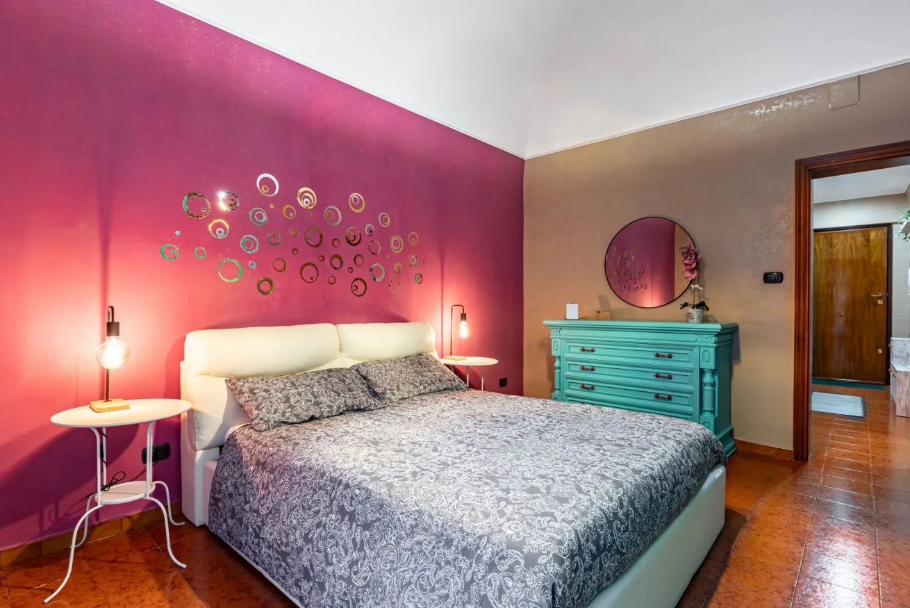 A bedroom with a bed, colorful wall decorations, and a turquoise dresser.