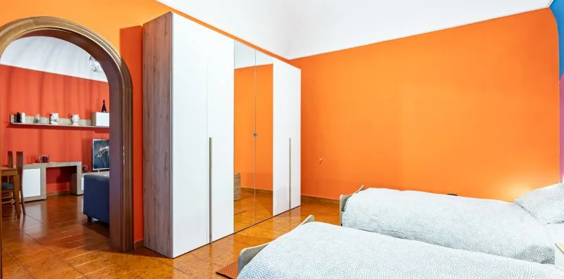 A bedroom with bright orange walls, a wardrobe, and beds.