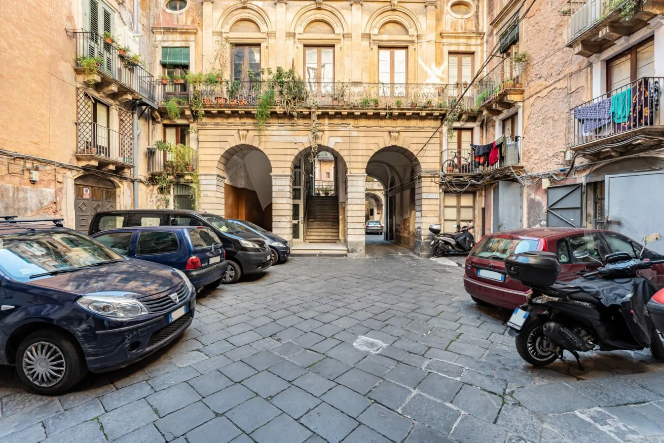 A paved courtyard between apartment buildings, with parked cars and balconies.