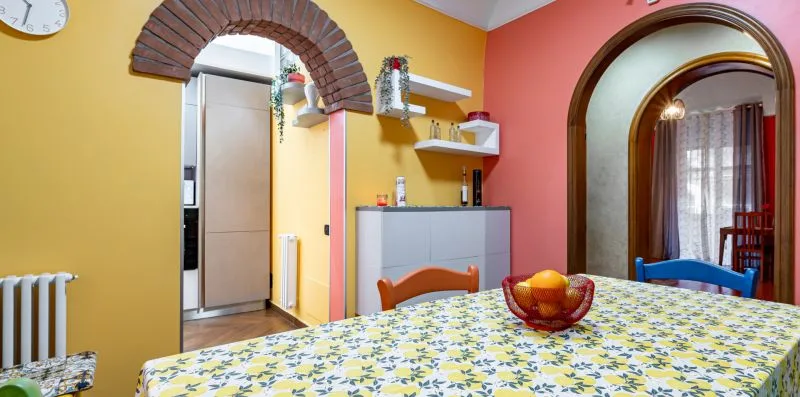 A dining area with a patterned tablecloth and an arched doorway opening to a sitting area.