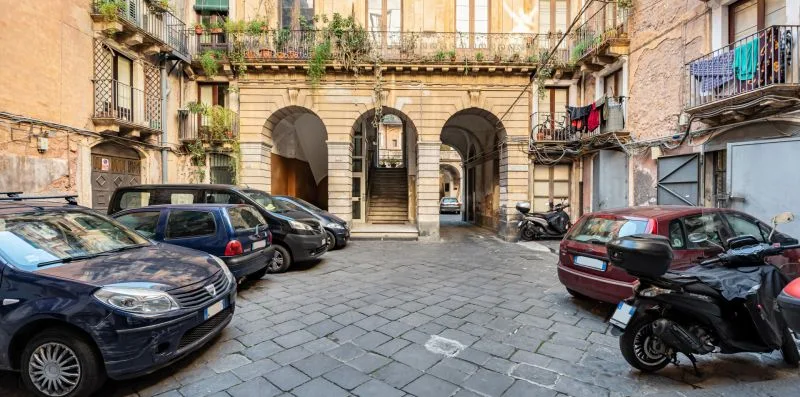 A paved courtyard parking area is surrounded by buildings with arched passages.
