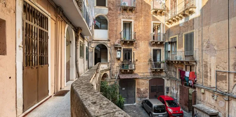 A narrow stone walkway overlooks a small courtyard between old apartment buildings.