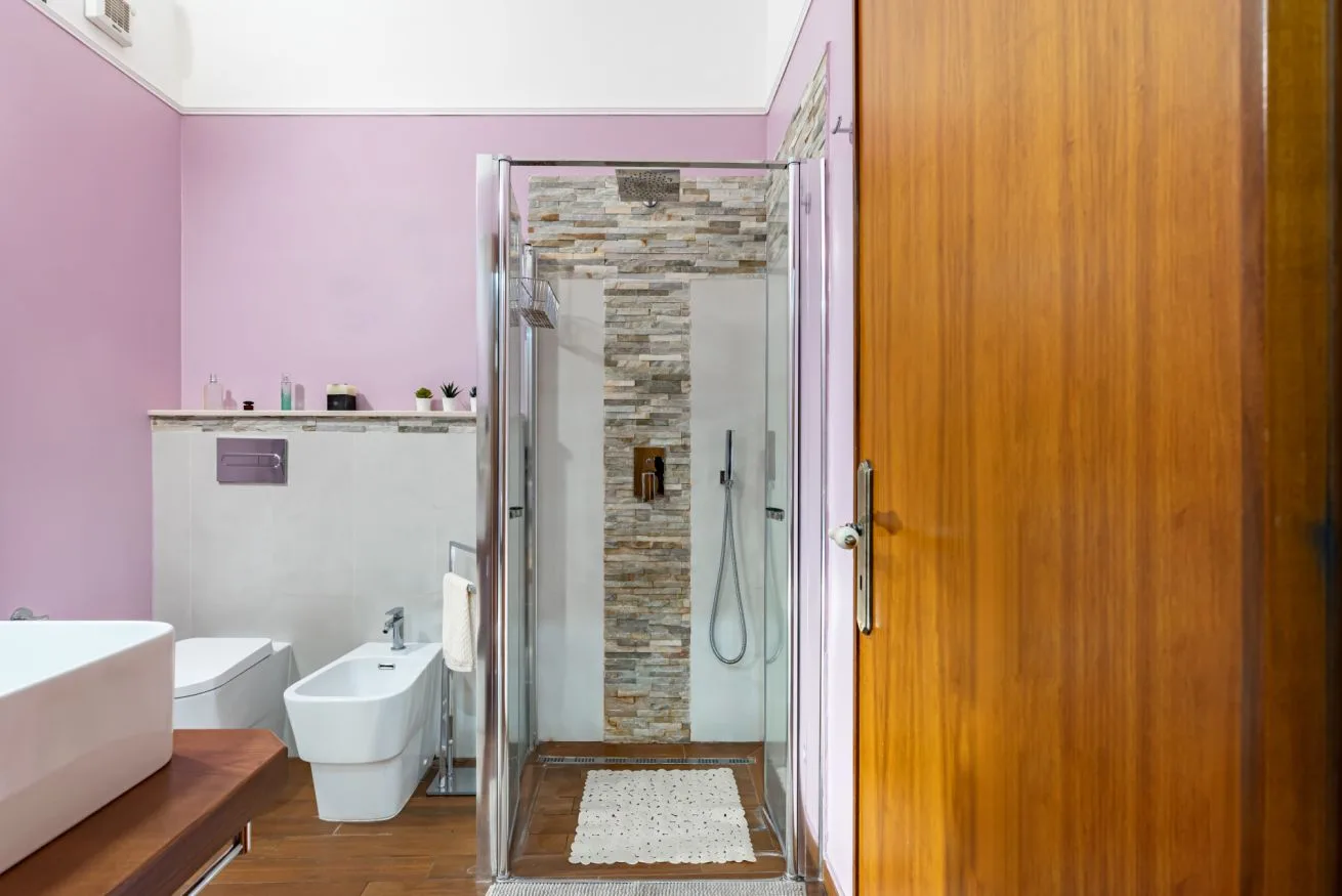 A bathroom with a glass shower and a wood-finished door.