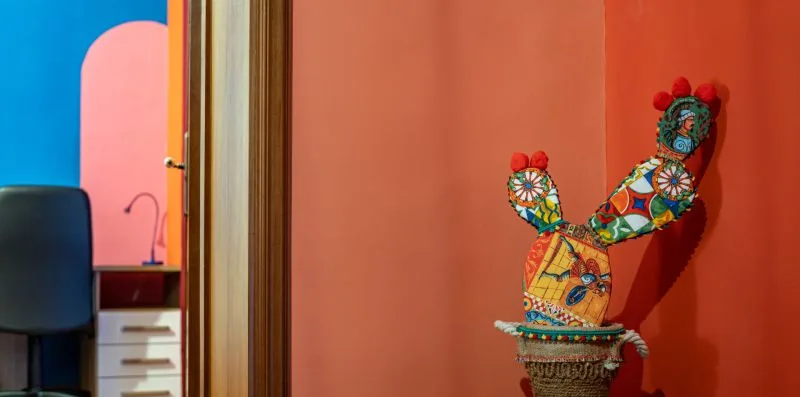 A colorful decorative sculpture stands against a coral-colored wall.