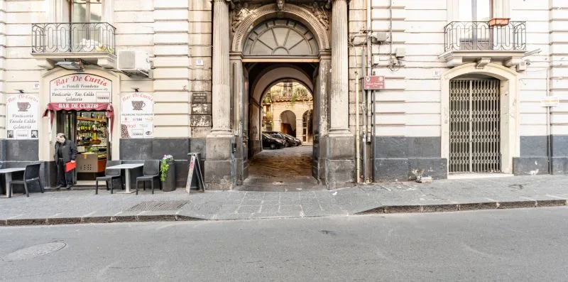 A city street with a large arched building entrance and storefronts.