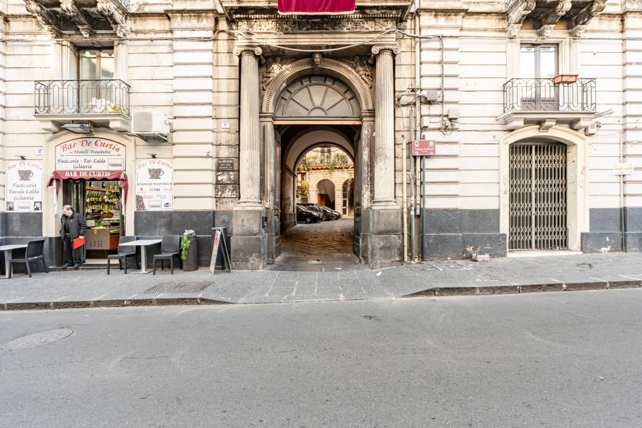 A street-facing building entrance with a large arched passage and a café beside it.