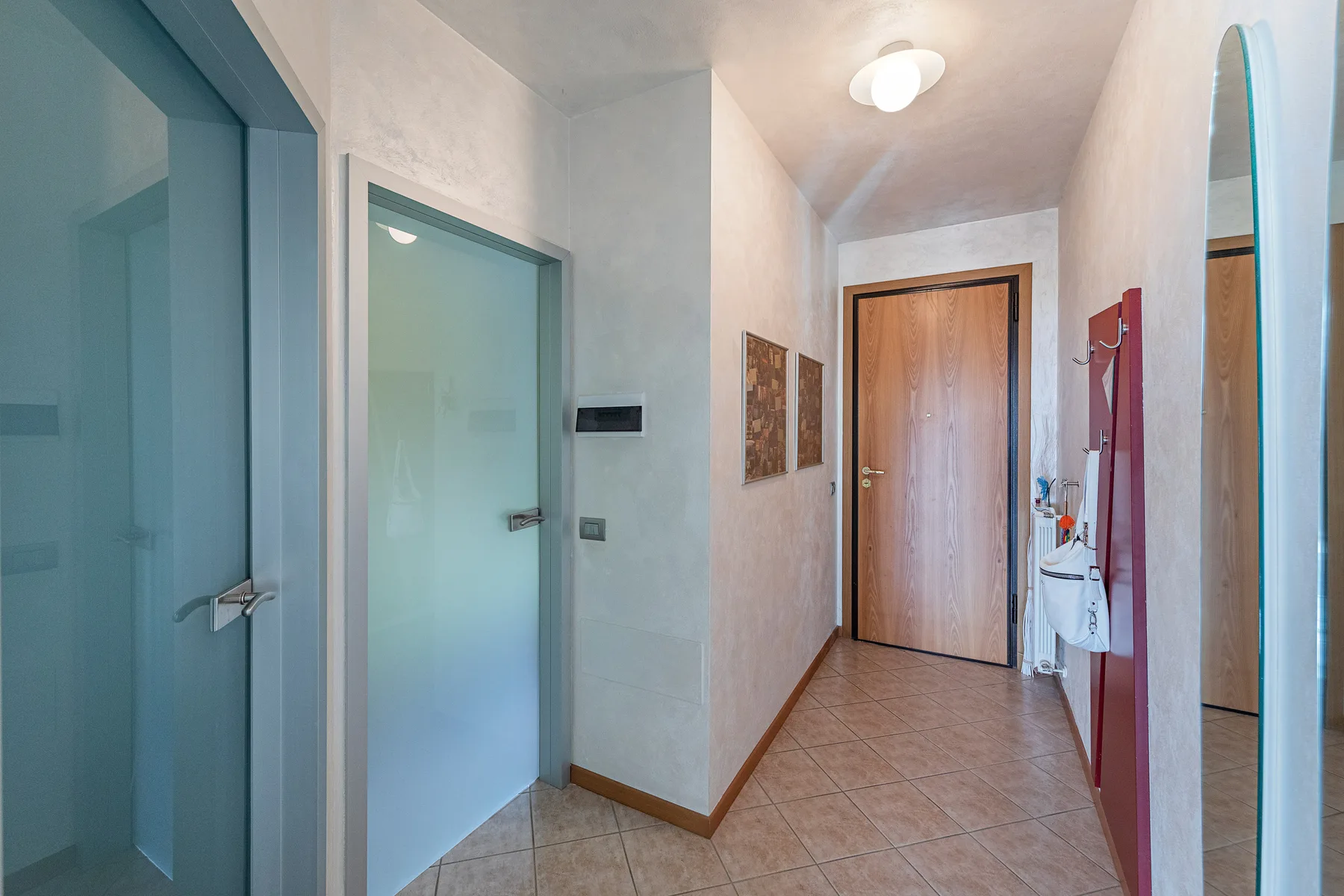 Un pasillo estrecho con una puerta de madera al fondo y puertas de vidrio esmerilado.