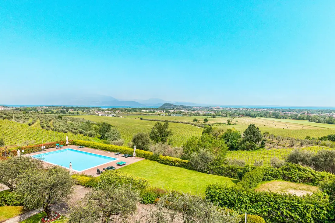 Una piscina está rodeada de campos verdes y árboles bajo un cielo despejado.