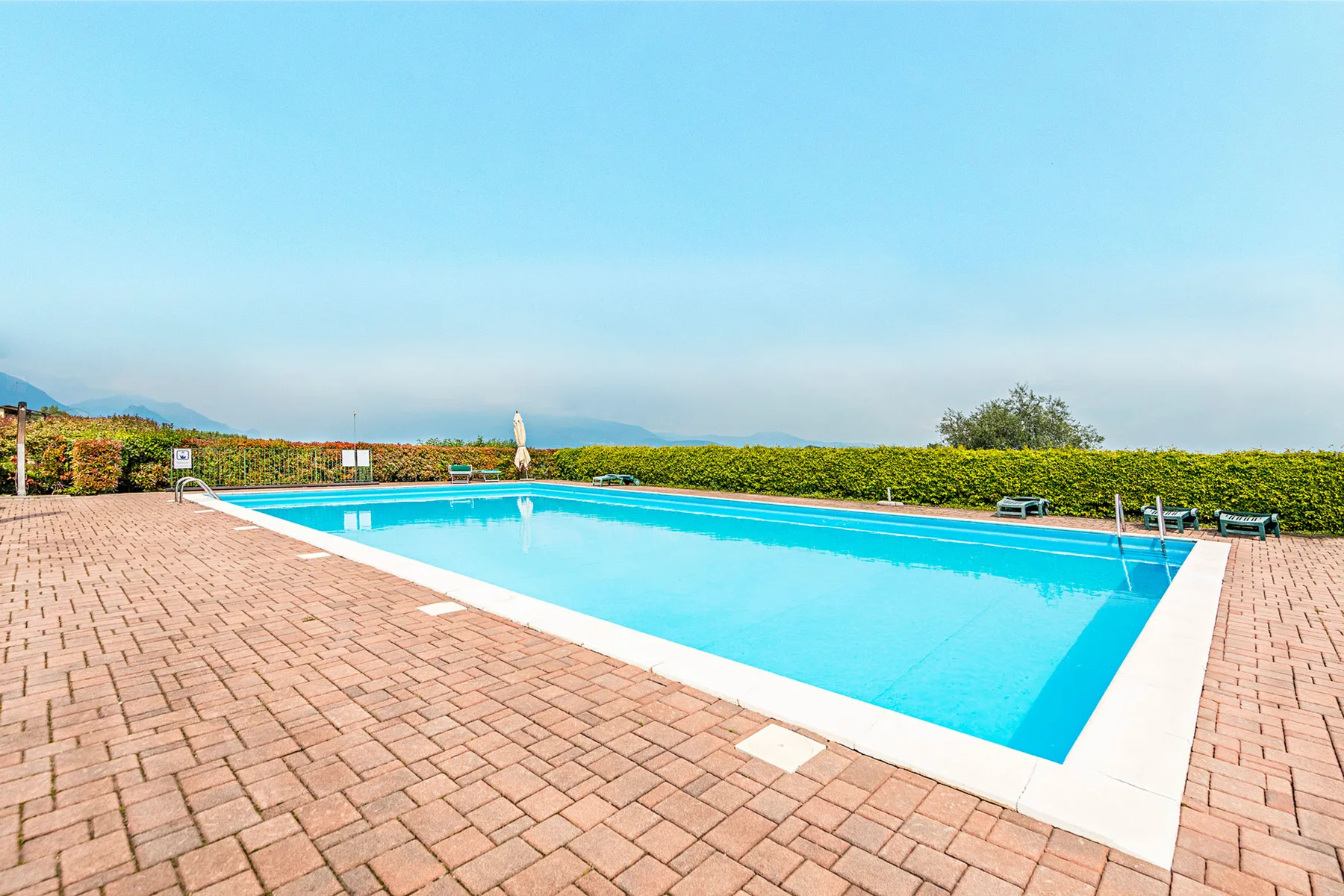 Una piscina al aire libre está rodeada por una terraza de ladrillo y vegetación.