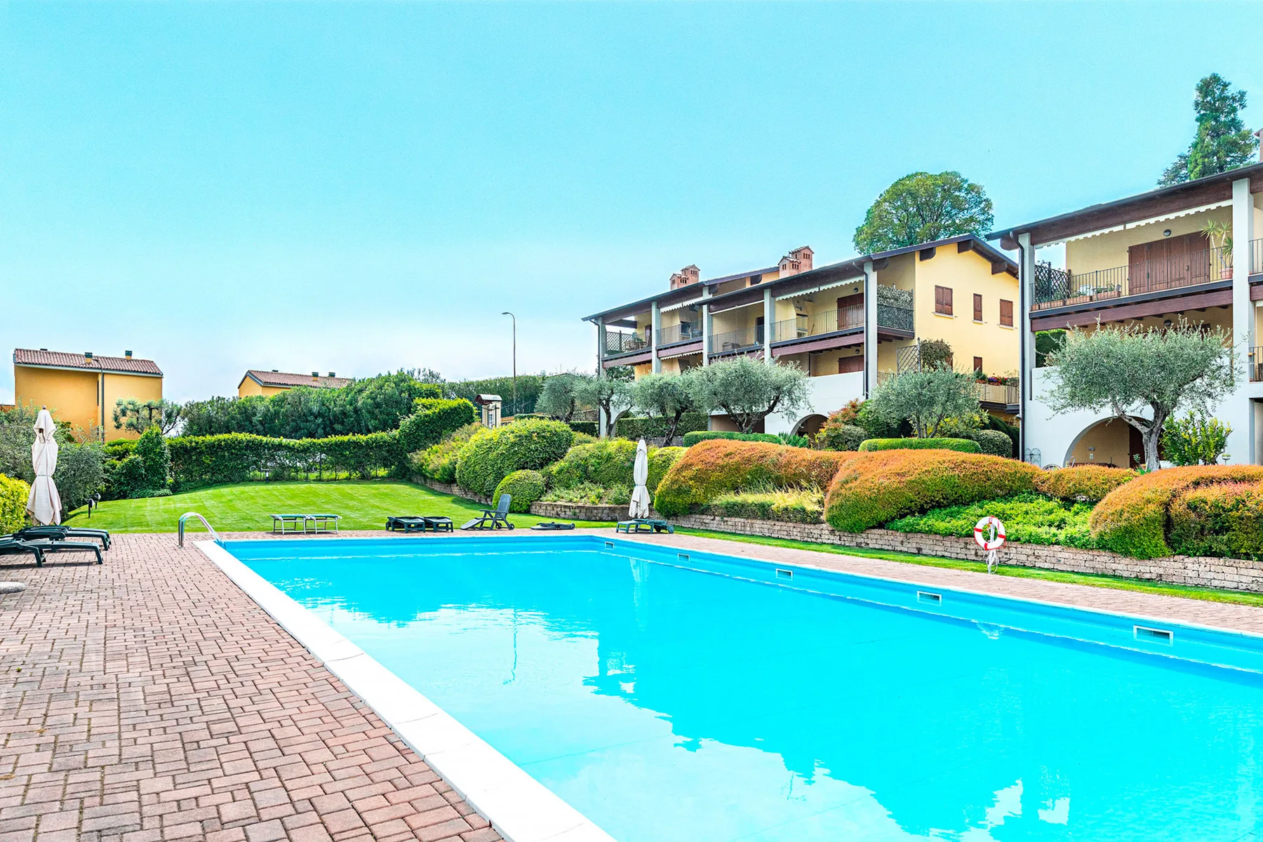 Piscina al aire libre junto a una terraza pavimentada y jardines.