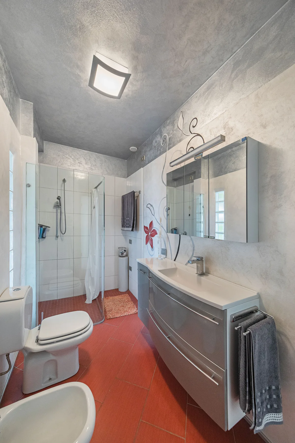 Un baño alicatado con ducha, inodoro y un mueble de lavabo alargado.