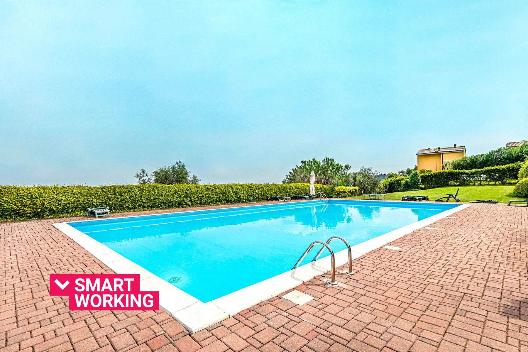 Una piscina al aire libre está rodeada por una terraza de ladrillo y setos recortados.