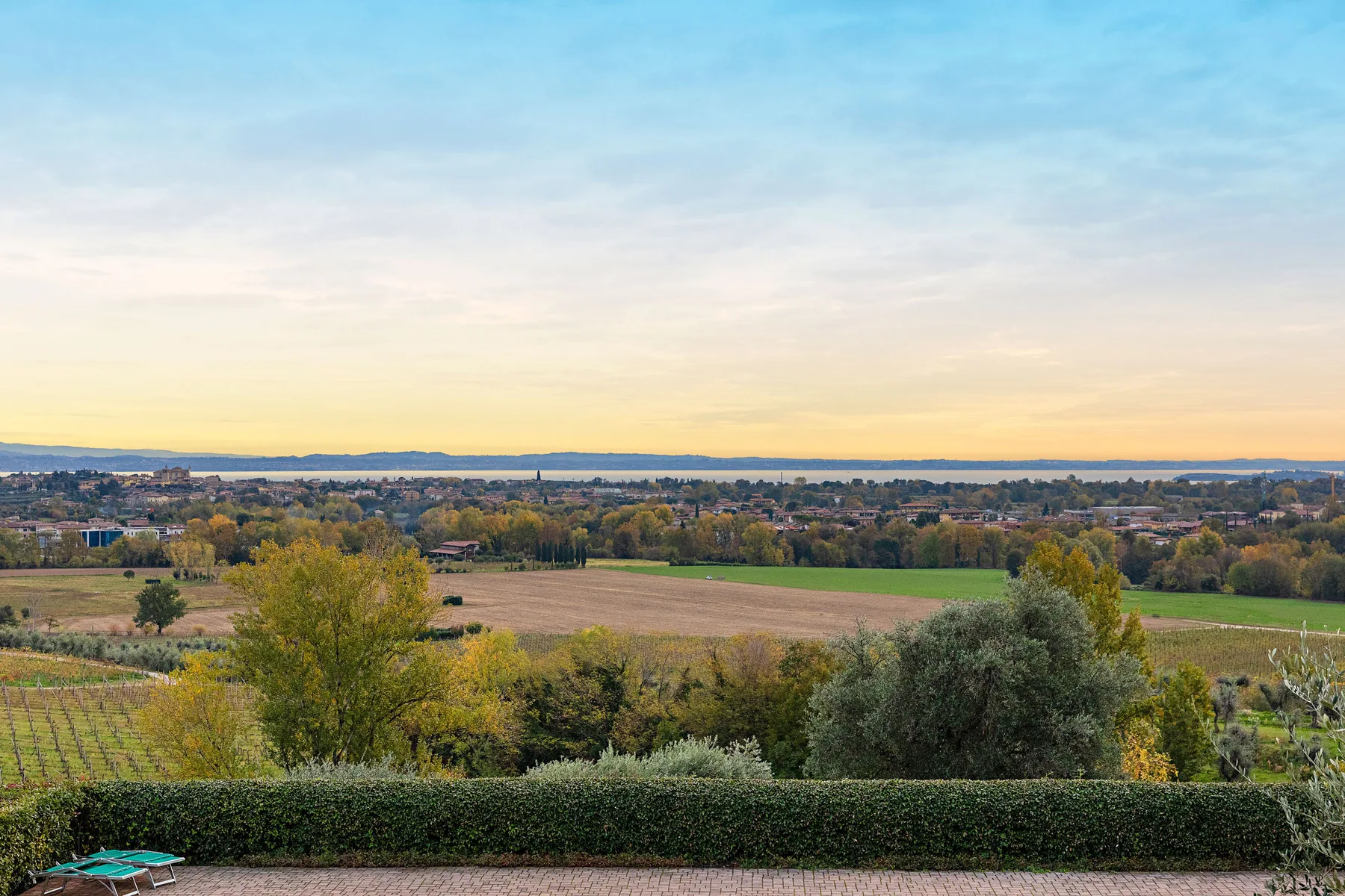 Una vista amplia del paisaje muestra campos, árboles y edificios lejanos bajo un cielo colorido.