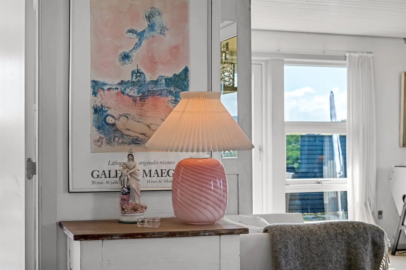 Una sala luminosa con una lámpara rosa junto a la ventana.