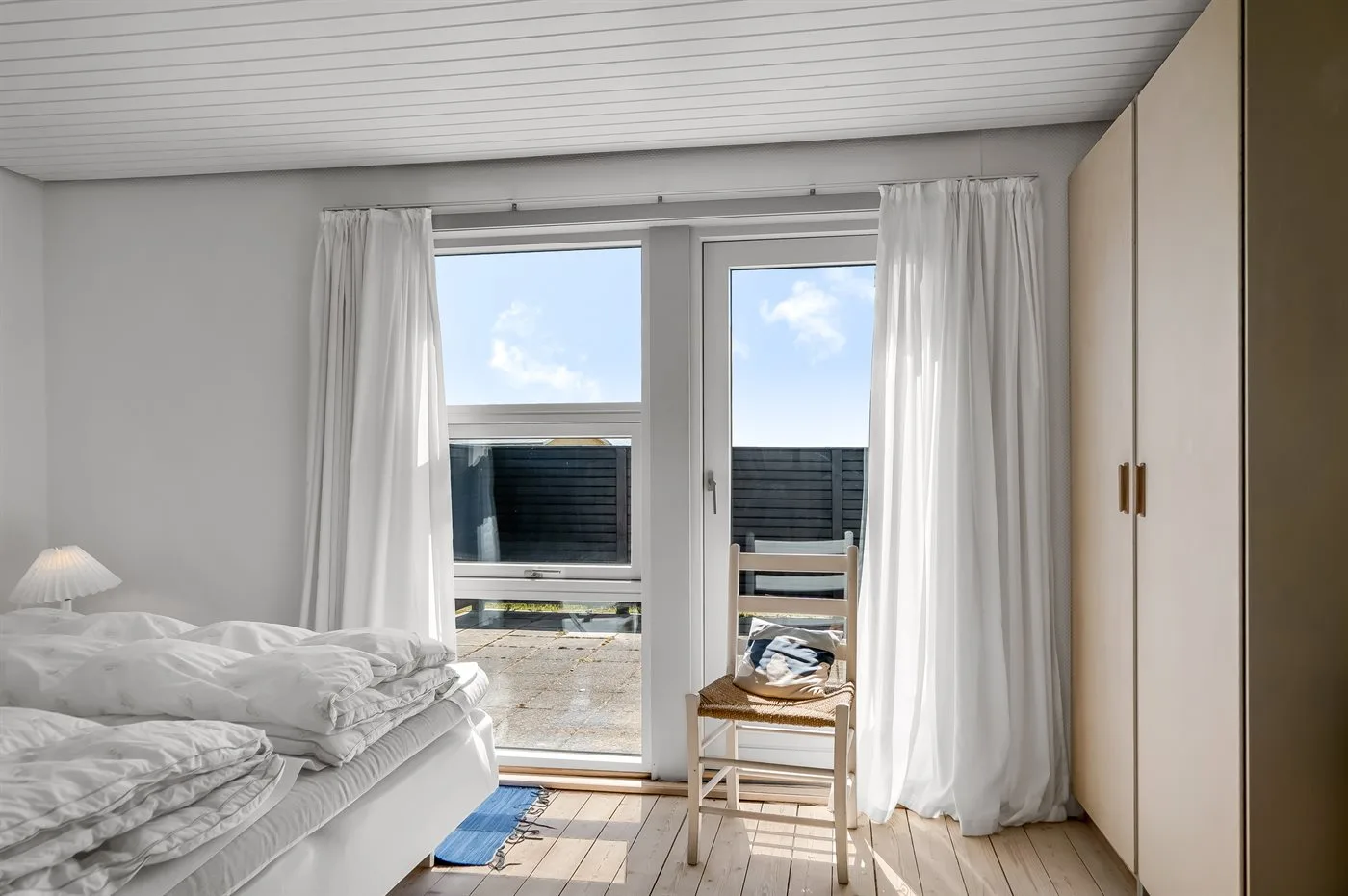 Un dormitorio luminoso con una cama junto a una puerta de vidrio y una ventana.