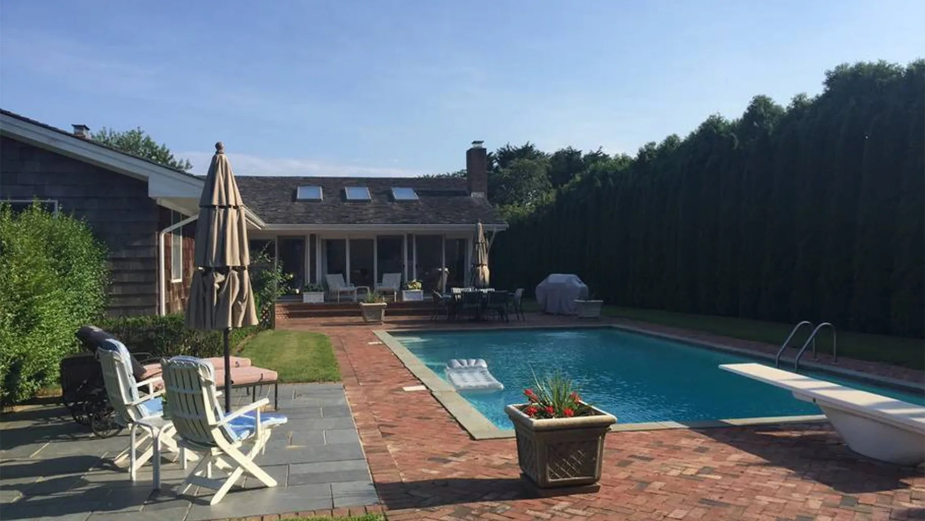 Una piscina al aire libre junto a un patio con asientos y vegetación.