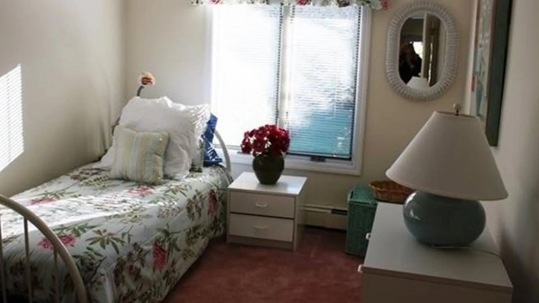 Un dormitorio con una cama cubierta con flores junto a una ventana luminosa.