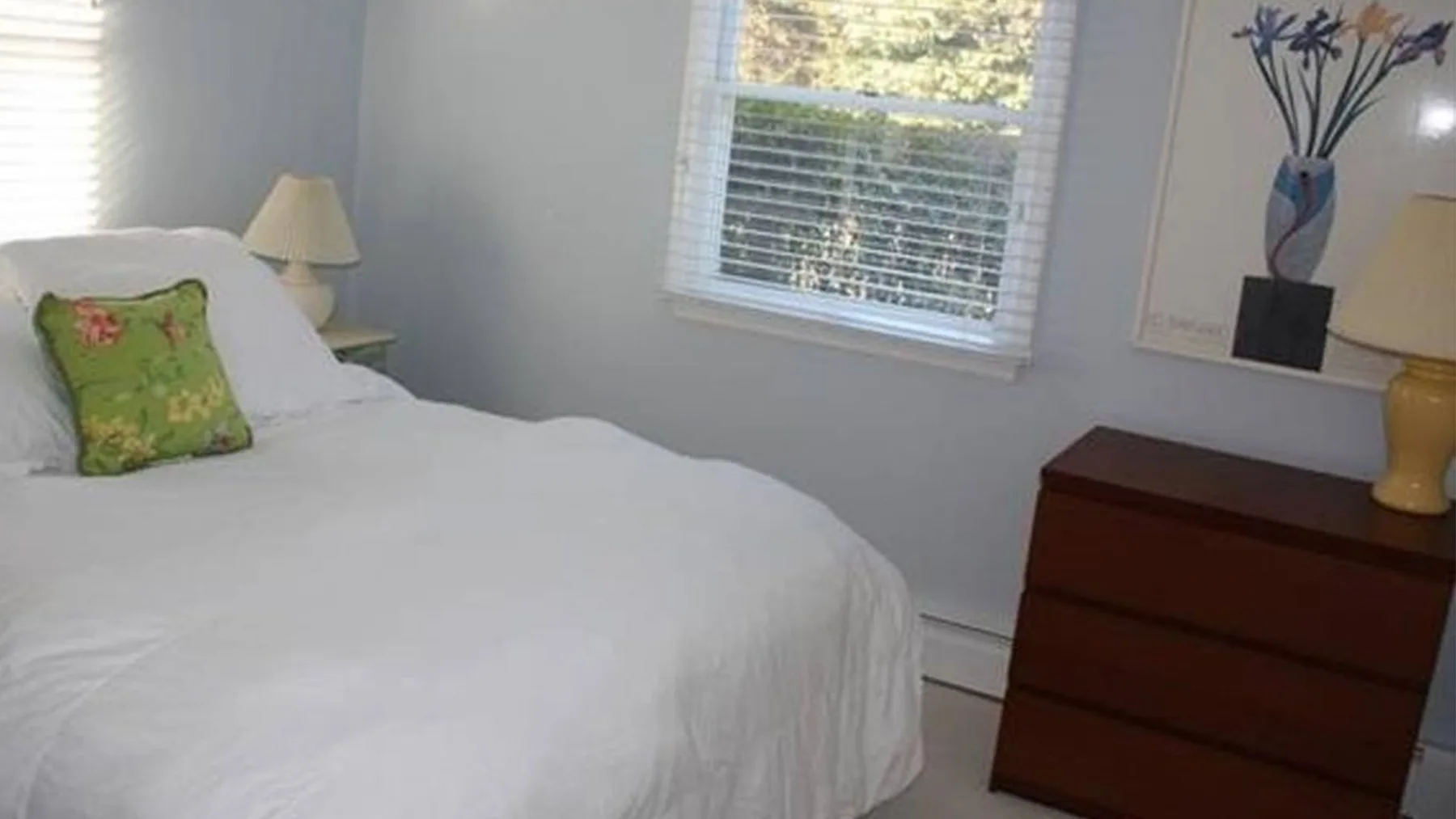 Un dormitorio con una cama blanca, una ventana y una cómoda de madera.