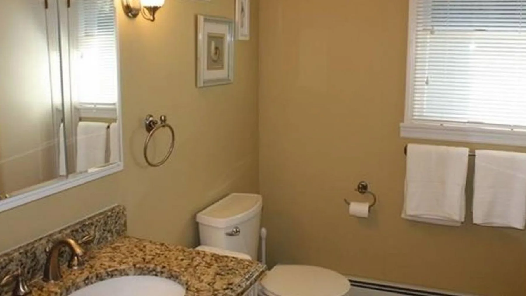 Un baño con lavabo, inodoro y toallas colgadas bajo una ventana.