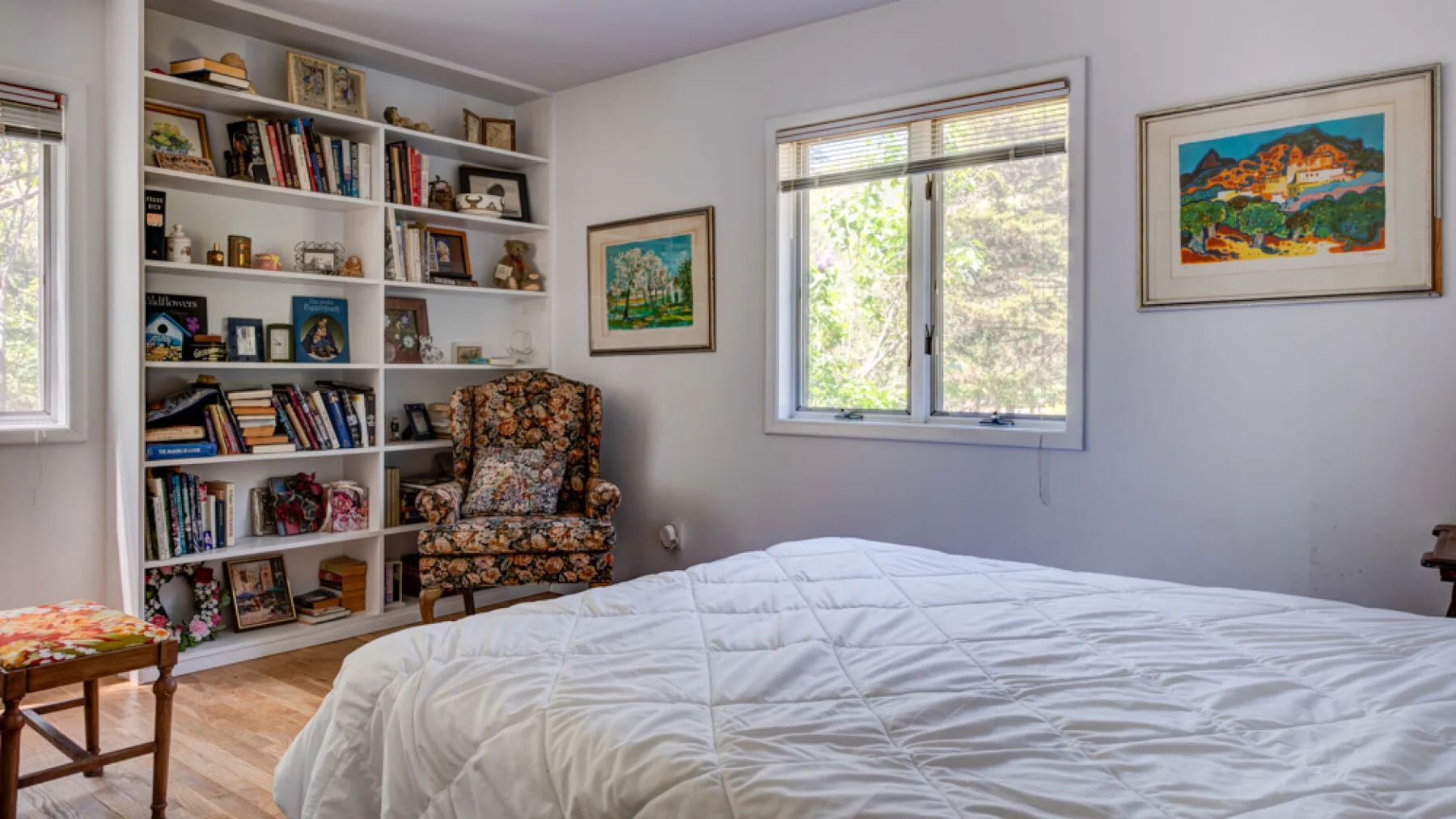 A bedroom with a bed, a bookcase, and a patterned armchair.
