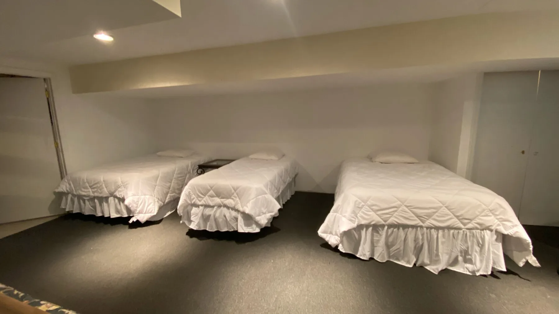 A low-ceiling bedroom with white bedding and several sleeping spaces.