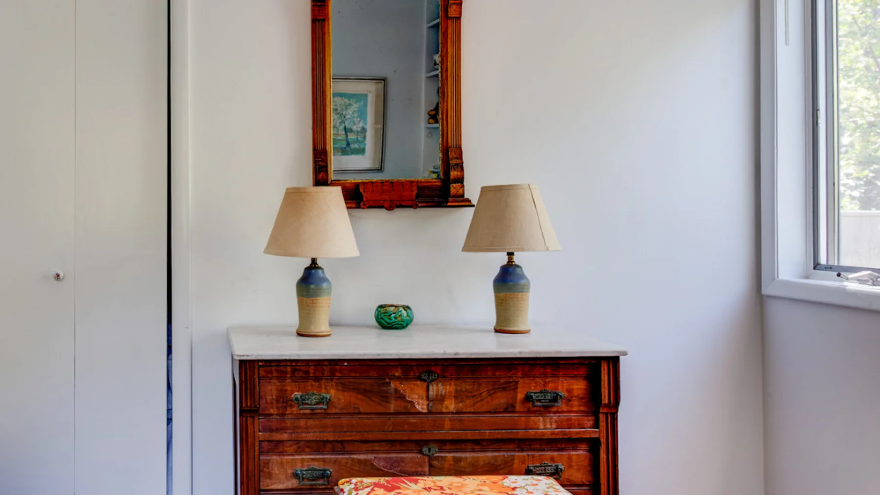 A wooden dresser with two lamps stands beneath a mirror.