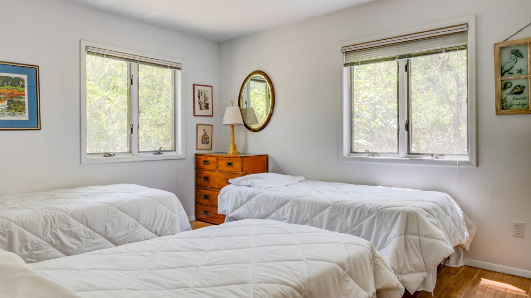 A bright bedroom with beds dressed in white bedding and windows overlooking greenery.