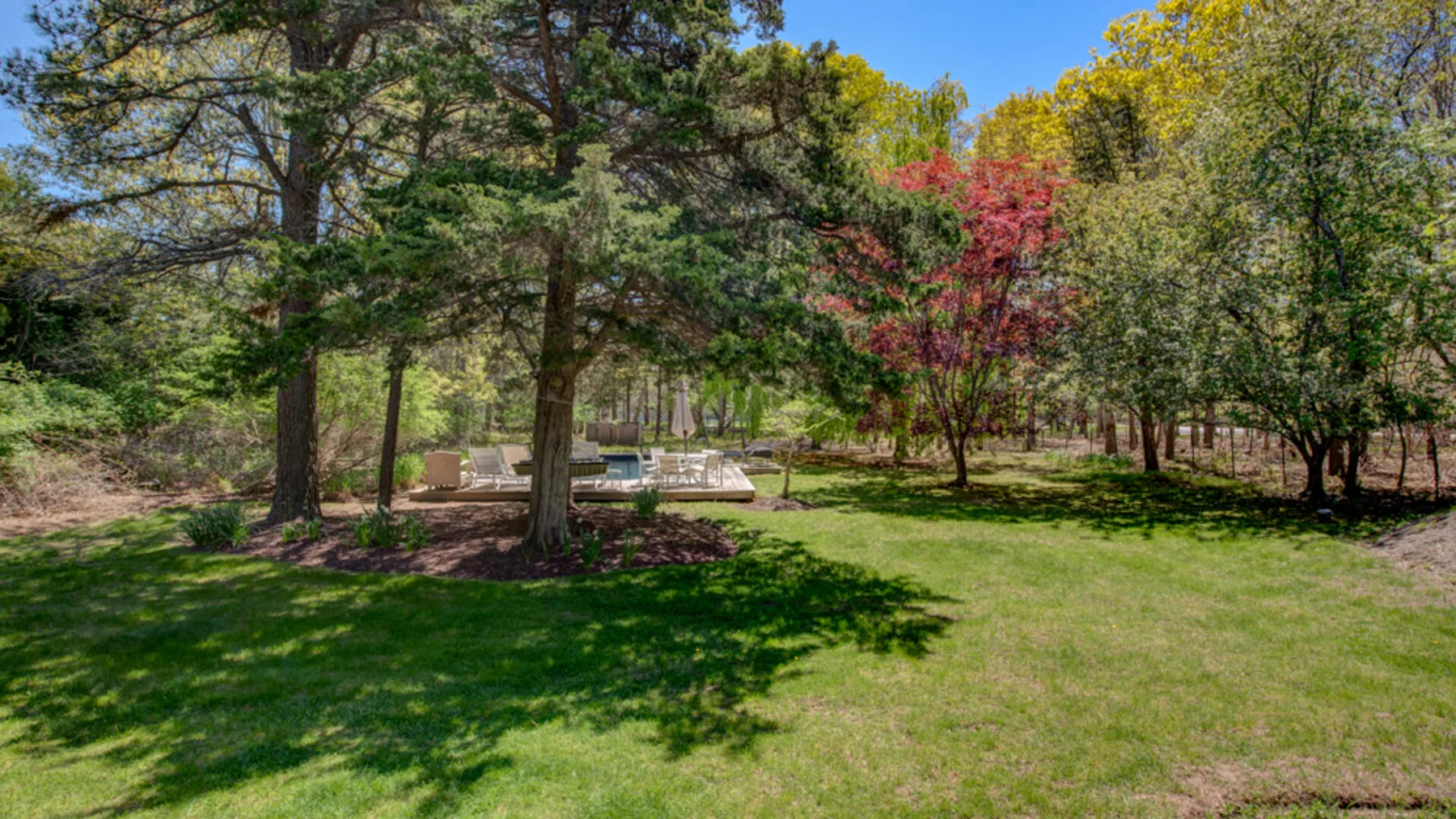 A grassy yard with mature trees and a small seating area.