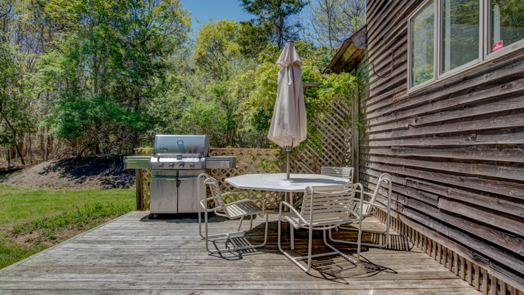 A wooden deck beside a house has a patio table, seating, and a grill.