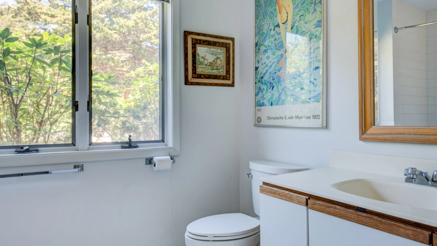 A bathroom with a sink, toilet, and window overlooking greenery.
