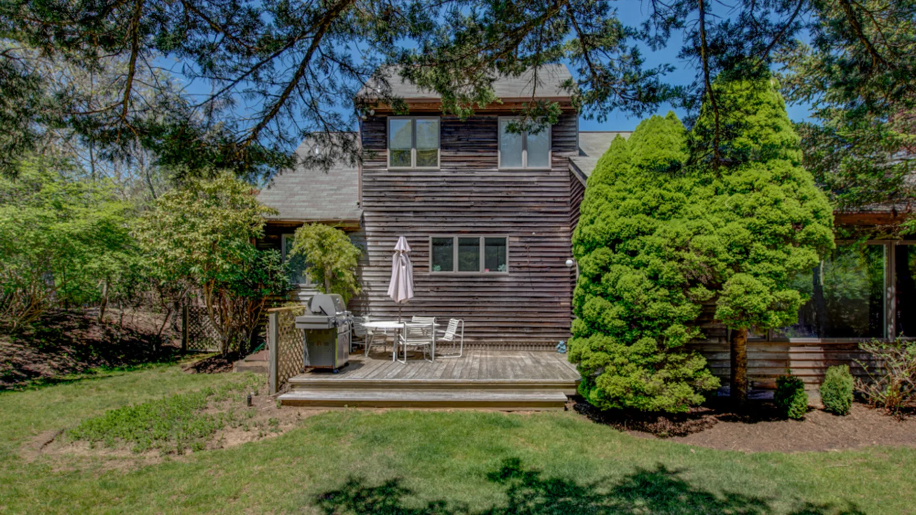 A wooded yard with a two-story house and a small patio.