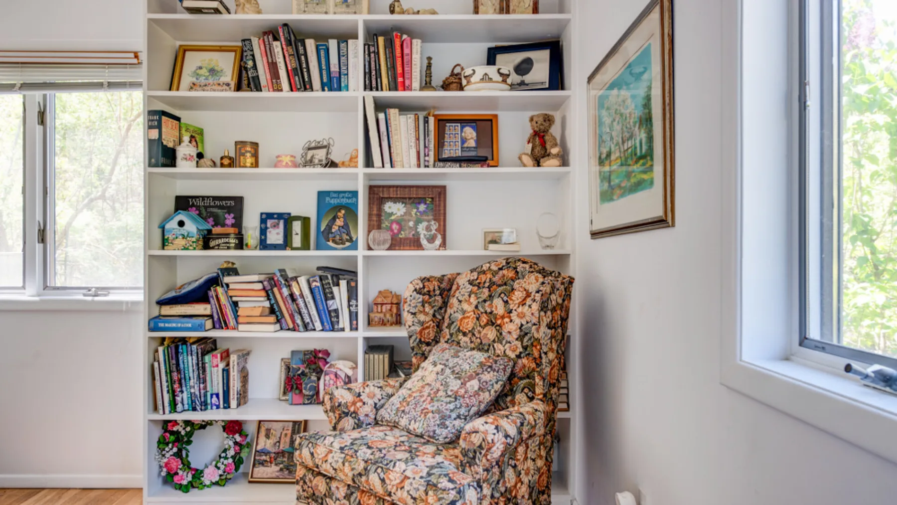 A floral upholstered armchair sits in front of a bookcase filled with books and decor.
