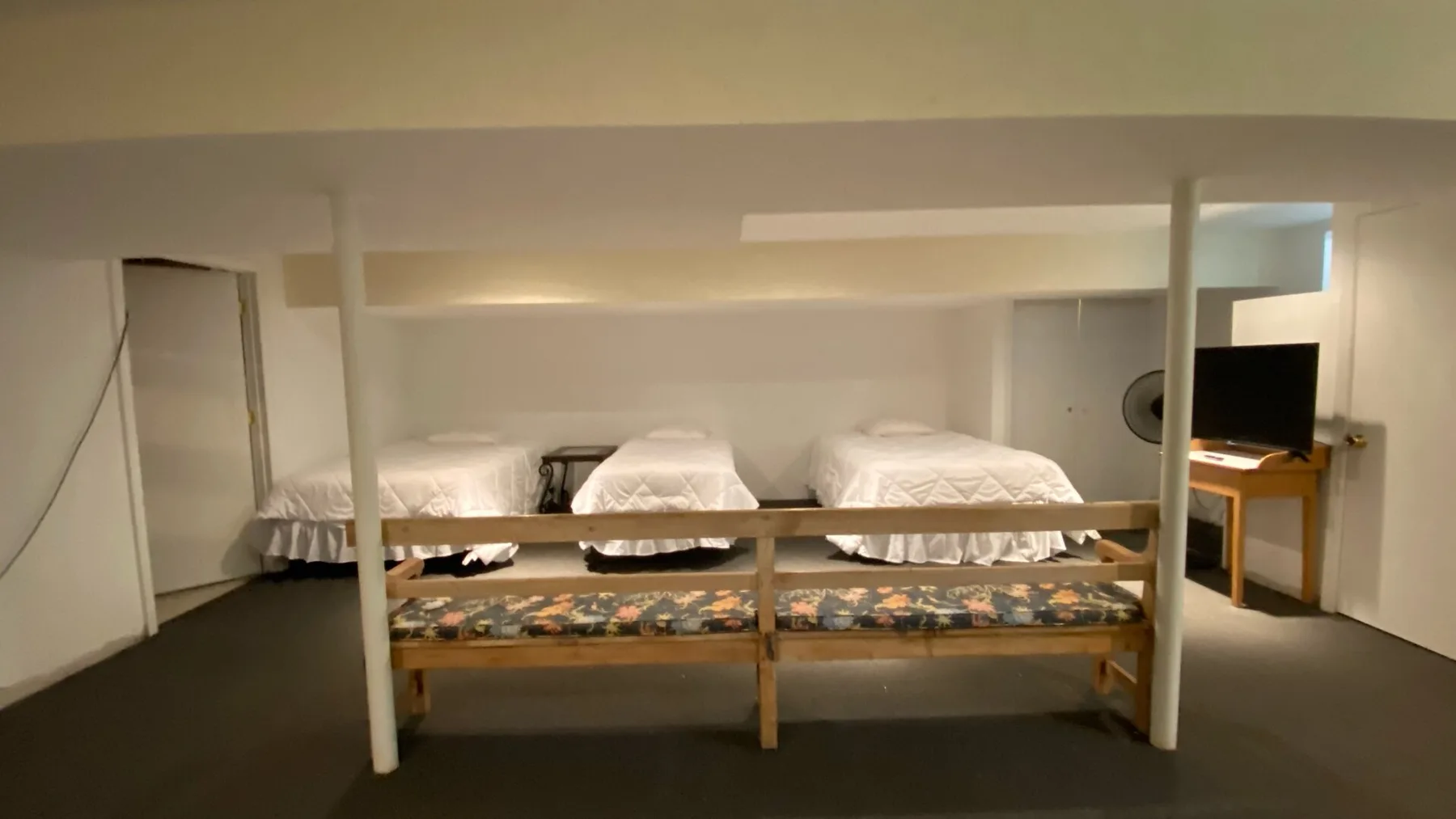 A low-ceiling sleeping area has several beds and a small television.