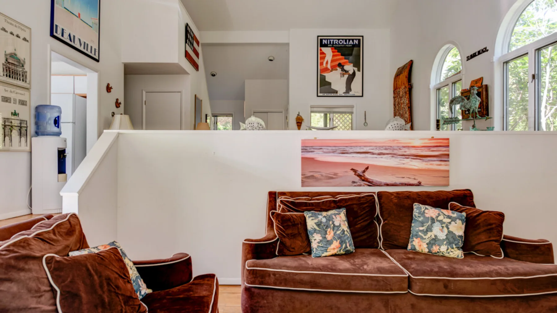 A bright living room has brown seating and a large sunset print above it.