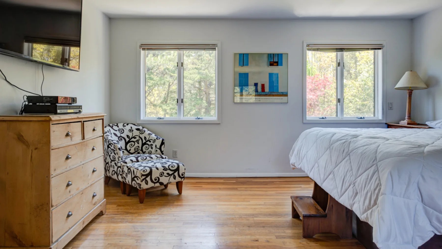 A bedroom with a bed, patterned armchair, and wooden dresser.